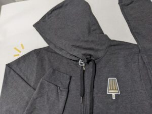 En mörkgrå hoodie med tryck av en glasspinne på bröstet.